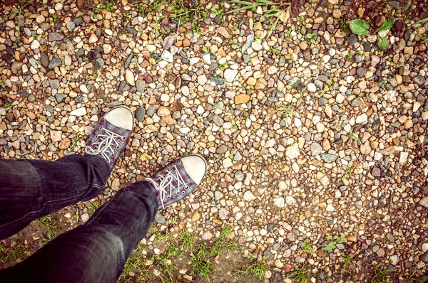 Background feet in sneakers and jeans are on pebbles — Stock Photo, Image