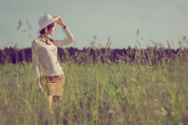 Flicka i vit cowboyhatt leende och hålla hatten på gr — Stockfoto