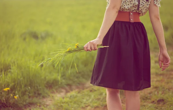Kız elbise bir alanda yürüyüş arka plan ve karahindiba tutun — Stok fotoğraf