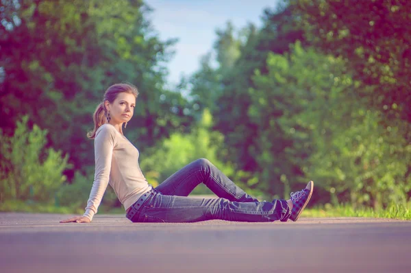 Pozadí dívka sedící na asfaltovou silnici mezi zelenými stromy v — Stock fotografie