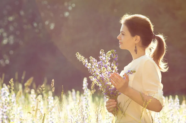 手に花を持つフィールドで夏の背景の女の子 — ストック写真