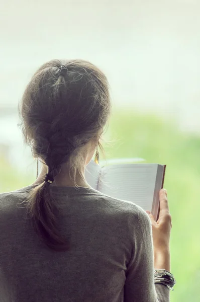 Menina de fundo de pé na janela, segurando um caderno aberto — Fotografia de Stock