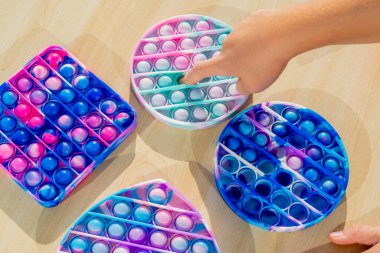 Stres önleyici aletlerle oynayan küçük bir çocuk tahta masaya koyuyor. El ele tutuşup gökkuşağı renginde popit çalıyoruz. 2021 yılının trendi. Üst Manzara. Yüksek kalite fotoğraf