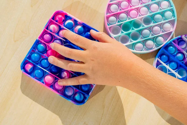 Stres önleyici aletlerle oynayan küçük bir çocuk tahta masaya koyuyor. El ele tutuşup gökkuşağı renginde popit çalıyoruz. 2021 yılının trendi. Üst Manzara. Yüksek kalite fotoğraf