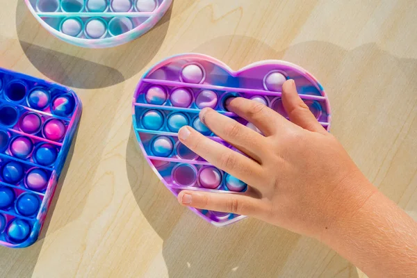 Stres önleyici aletlerle oynayan küçük bir çocuk tahta masaya koyuyor. El ele tutuşup gökkuşağı renginde popit çalıyoruz. 2021 yılının trendi. Üst Manzara. Yüksek kalite fotoğraf