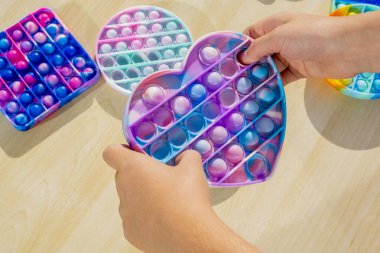 Stres önleyici aletlerle oynayan küçük bir çocuk tahta masaya koyuyor. El ele tutuşup gökkuşağı renginde popit çalıyoruz. 2021 yılının trendi. Üst Manzara. Yüksek kalite fotoğraf