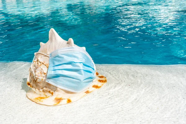 Uma concha grande com máscara protetora perto da piscina. Férias durante o COVID-19 com conceito de máscara protetora — Fotografia de Stock
