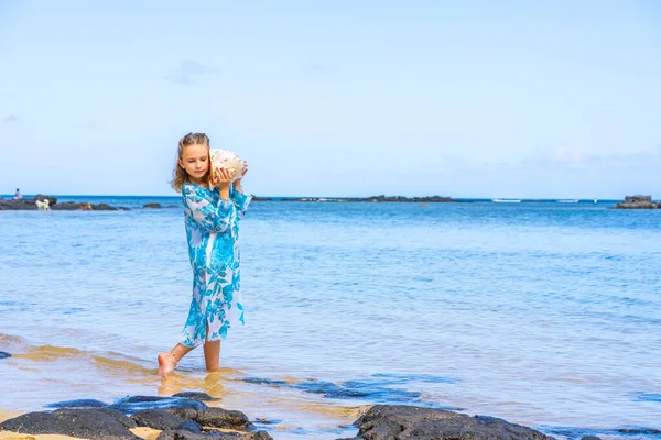 Ein Mädchen, das am tropischen Sommerstrand eine riesige Muschel in der Nähe hält und hört — Stockfoto