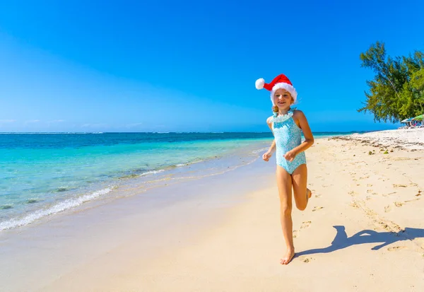 Tropikal yaz plajında koşan Noel şapkalı güzel bir kız. Tropik ada konseptinde kış tatili. Yüksek kalite fotoğraf