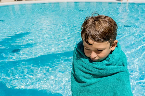 Ragazzo avvolto in asciugamano sensazione di freddo dopo aver nuotato in piedi accanto alla piscina. — Foto Stock