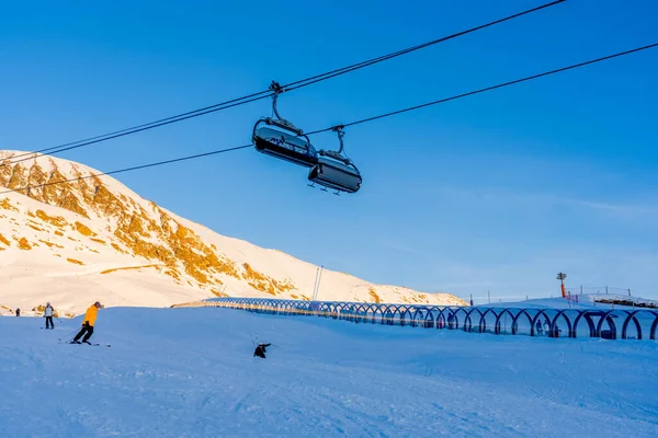 Alpe dHuez, France - 30.12.2021 : Ski lift ropeway on alpine mountain winter resort on the evening. Ski chairlift cable way with people. Typical french winter season landscape. — Stock Photo, Image