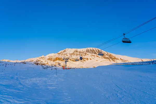 Alpe dHuez, France - 30.12.2021 : Ski lift ropeway on alpine mountain winter resort on the evening. Ski chairlift cable way with people. Typical french winter season landscape. — Stockfoto