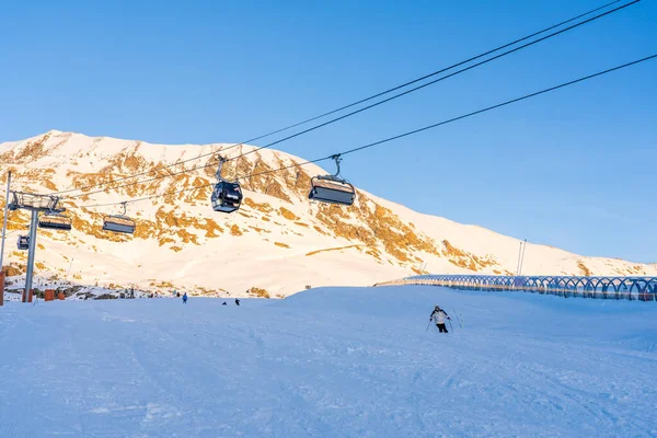 Alpe dHuez, França 30.12.2021: Ropeway elevador de esqui na montanha alpina resort de inverno à noite. Cadeira de esqui maneira de cabo com as pessoas. Paisagem típica da época de inverno francesa. — Fotografia de Stock