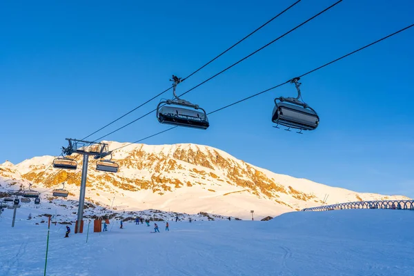 Alpe dHuez, France - 30.12.2021 : Ski lift ropeway on alpine mountain winter resort on the evening. Ski chairlift cable way with people. Typical french winter season landscape. — Foto Stock