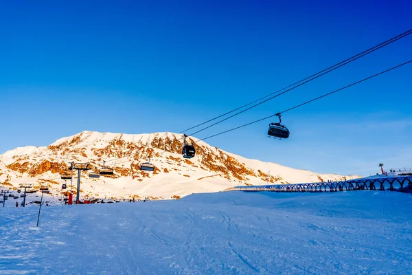 Alpe dHuez, França 30.12.2021: Ropeway elevador de esqui na montanha alpina resort de inverno à noite. Cadeira de esqui maneira de cabo com as pessoas. Paisagem típica da época de inverno francesa. — Fotografia de Stock