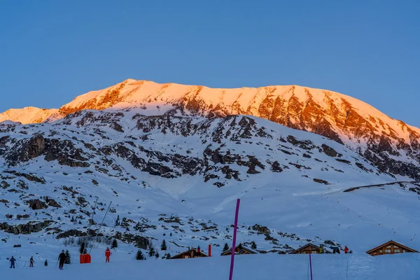Alpe dHuez, Frankrijk - 30.12.2021: Winterlandschap op alpine bergen resort in de avond. Skiërs op de skipiste. — Stockfoto