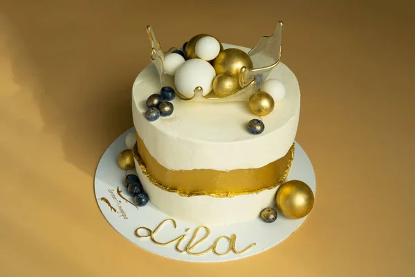 Een prachtige verjaardagstaart, versierd met goud en witte kleuren met ballen in een gekarameliseerde transparante mand op de top. Het concept van feestelijke desserts Rechtenvrije Stockafbeeldingen