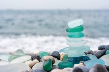 Deniz kıyısındaki doğal cilalı cam ve taşlar. Dalgalı açık deniz suyu. Yakından bakınca çok renkli deniz taşları olan yeşil, parlak camlar. Plaj yaz geçmişi