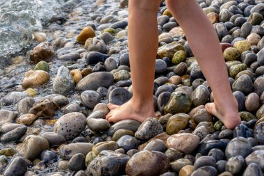 Bir kız ayakları denizin çakıl taşlı sahillerinde yürür. Kızların bacakları kapalı. Kaliteli fotoğraf