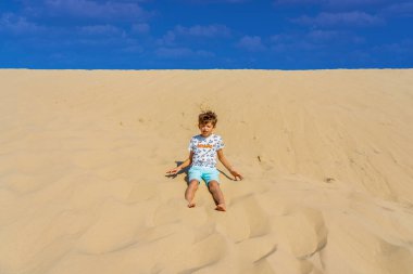 Boy sitting on a huge sand dune, famous tourist destination Dune Pyla. Pilat Dune in France. High quality photo
