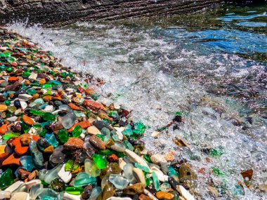 Deniz kıyısındaki doğal cilalı cam ve taşlar. Dalgalı açık deniz suyu. Yakından bakınca çok renkli deniz taşları olan yeşil, parlak camlar. Plaj yaz geçmişi
