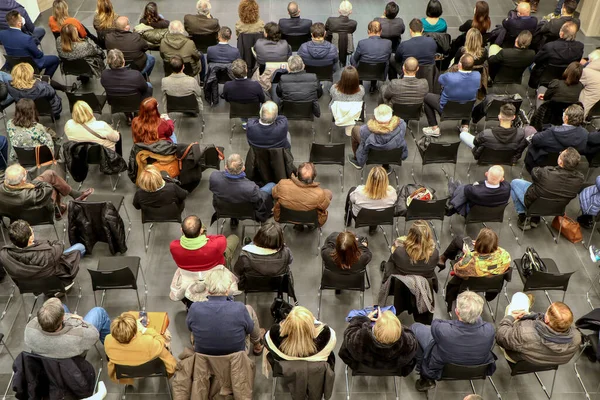 Group view of seated people, unrecognizable men and women, viewed from above and from behind