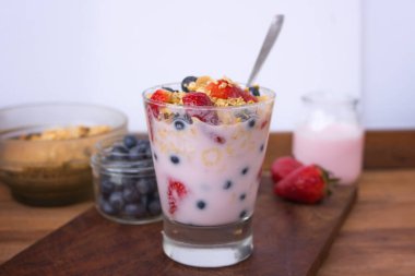 Yoğurtlu cam, tahıl gevreği, çilek ve ahşap yaban mersini.