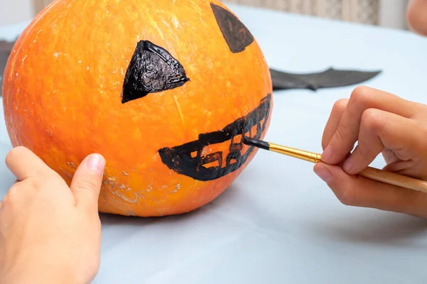 Χέρι σχεδιάζει ένα τρομακτικό πρόσωπο σε μια πορτοκαλί κολοκύθα με ένα πινέλο για να δημιουργήσετε ένα Halloween Jack Lantern, κοντινό πλάνο — Φωτογραφία Αρχείου