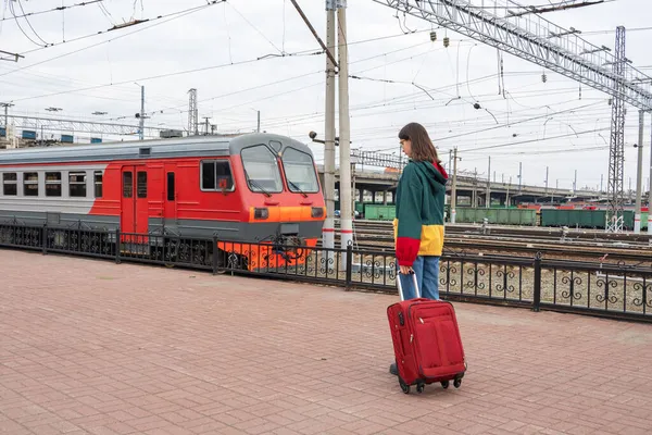 Vit flicka student i ljusa kläder med en resväska på väg till det elektriska tåget på stationen. — Stockfoto