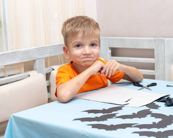 Un niño dibuja y corta una decoración de Halloween en casa de papel negro. Decoraciones de artesanía DIY. — Foto de Stock
