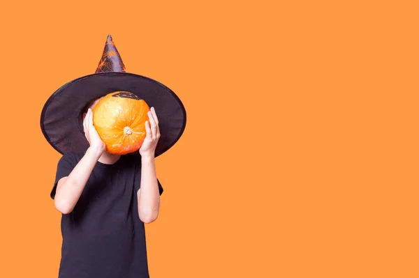 万圣节的孩子们一个戴着魔法帽的男孩在橙色的背景上把南瓜放在他的面前 复制空间 万圣节的心情 概念之间快乐的光环 — 图库照片
