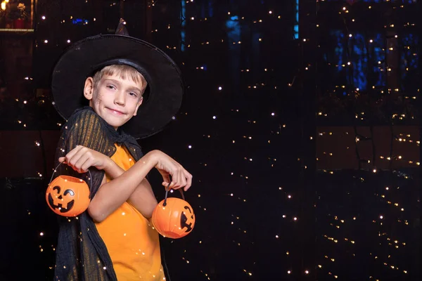 Pojke i trollkarlshatt och orange T-shirt håller Halloween pumpa-formade hinkar med godis — Stockfoto