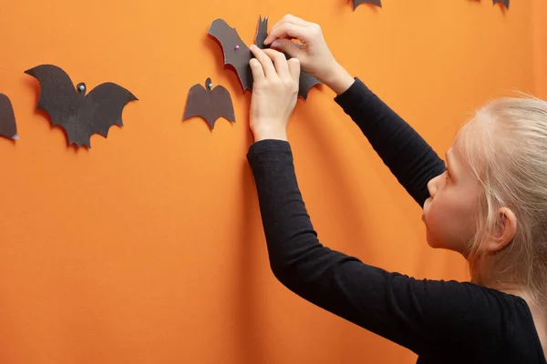 Halloween-ungar. Flicka hängande hemmagjord svart papper skuren bat på orange bakgrund. Halloweenstämning. — Stockfoto