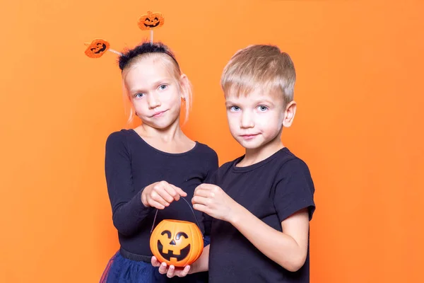 Trucs ou friandises pour enfants est une tradition d'Halloween. Garçon et fille tenant un panier orange en forme de citrouille avec des friandises — Photo