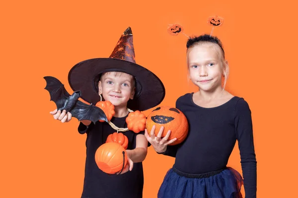 一个戴着魔法帽的小男孩拿着一个橙色的南瓜状篮子，一个黑色的球棒，一个拿着南瓜的女孩 — 图库照片