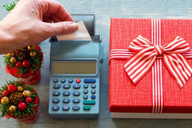 Elinde kurdeleli ve küçük Noel ağaçlı kırmızı hediye kutusunun yanındaki kasadan alınmış boş bir beyaz çek var.
