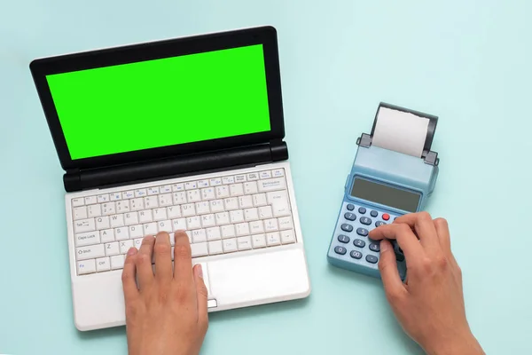 Ручная печать на ноутбуке с зеленым экраном и нажатие кнопок на кассовом аппарате на синем фоне — стоковое фото