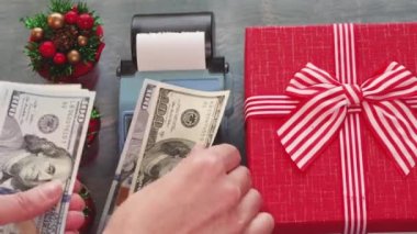 Kasiyerlerin elleri, kırmızı bir hediye kutusu ve küçük Noel ağaçlarının yanındaki kasada dolar sayıyor.
