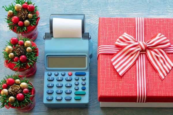 Venta de Navidad. Caja registradora, caja de regalo roja con cinta y pequeños árboles de Navidad con conos, primer plano, vista superior. Comprar regalos para Año Nuevo y Navidad — Foto de Stock