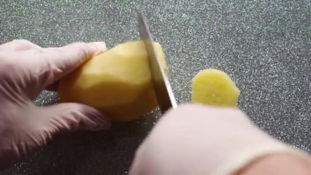 Chefs mãos em luvas cortando batatas com uma faca. Cortando batatas frescas em uma placa de corte preta close-up, Full HD. O conceito de cozinhar alimentos naturais saudáveis e saborosos em casa. — Vídeo de Stock