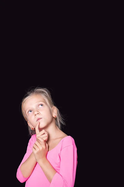 Pensativo hermosa chica caucásica en un suéter rosa mirando hacia arriba y sosteniendo su dedo en la cara sobre un fondo negro — Foto de Stock