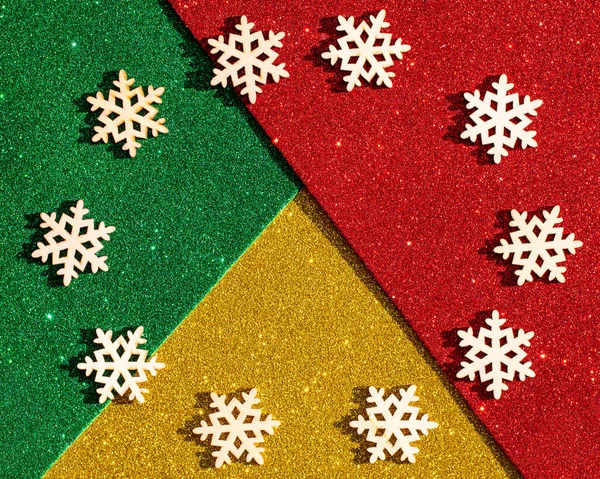 Wooden christmas snowflakes lying in a circle on a multicolored shiny green, red, gold background — Stock Photo, Image