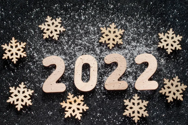 New Years concept - Ξύλινα νιφάδες χιονιού και αριθμοί 2022 πασπαλισμένα με χιόνι σε μαύρο αστραφτερό φόντο. Κάρτα Πρωτοχρονιάς. — Φωτογραφία Αρχείου