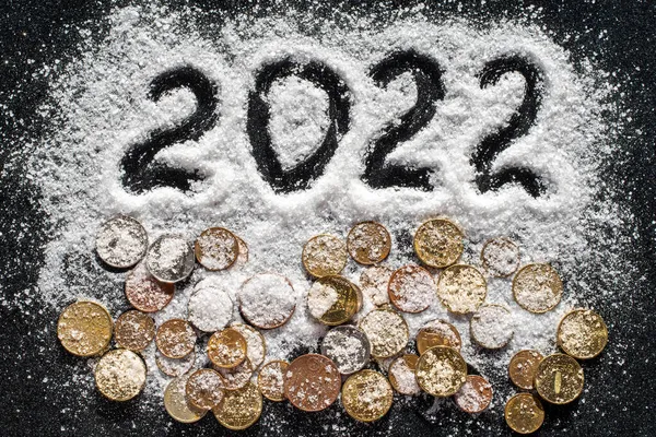 Χειρόγραφο έτος 2022 και διάφορα νομίσματα που καλύπτονται με λευκό θαλασσινό αλάτι, όπως το χιόνι σε μαύρο φόντο — Φωτογραφία Αρχείου