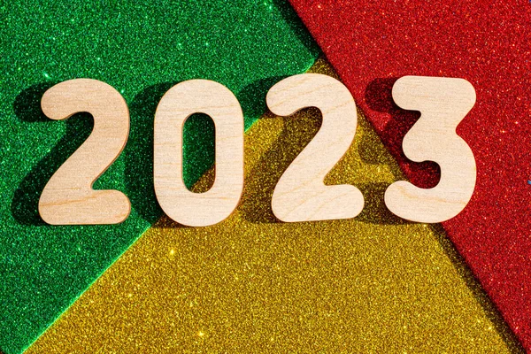 Wooden numbers 2023 on multicolored trending red, green, gold glittering starry background. New Year card. — Stock Photo, Image