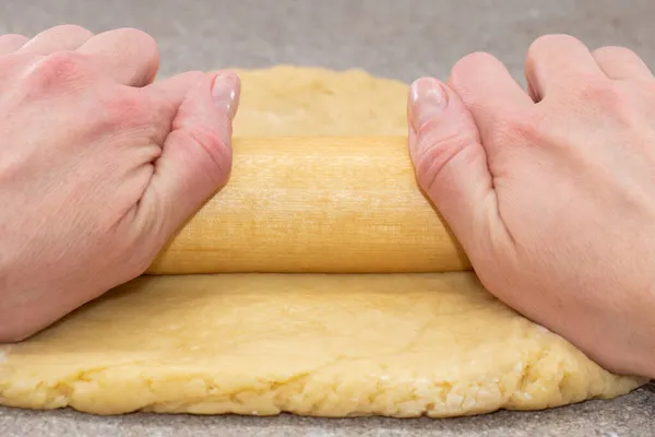 Chefs handen rollen het deeg uit met een deegroller op een grijze tafel, close-up. Deeg bakken voor taart, pizza, koekjes — Stockfoto