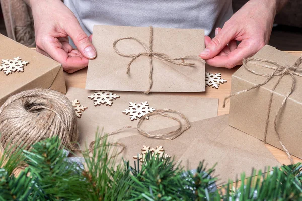 Manos sosteniendo un sobre de papel artesanal con una carta de Navidad en el fondo de regalos de Navidad y copos de nieve. — Foto de Stock
