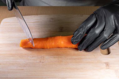 Şefin elleri siyah eldivenlerle bıçak tutuyor ve mutfak tahtasının üzerinde soyulmuş havuç doğruyor. Yakın plan. Salata hazırlama süreci. Doğal beslenme sağlıklı yiyecekler.