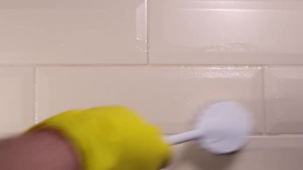 Mano masculina en un guante de goma amarillo limpiando la superficie de una baldosa de cerámica con un cepillo blanco. Eliminación de manchas, desinfección — Vídeo de stock