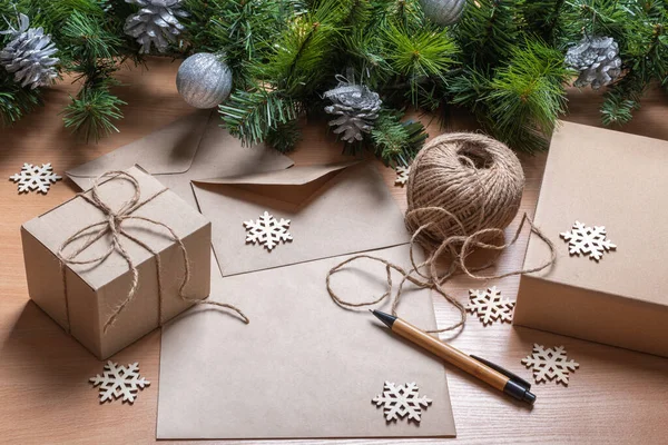 Hoja en blanco de papel, bolígrafo, regalos en cajas hechas a mano, cordel, ramas de abeto artificial y copos de nieve de madera. — Foto de Stock